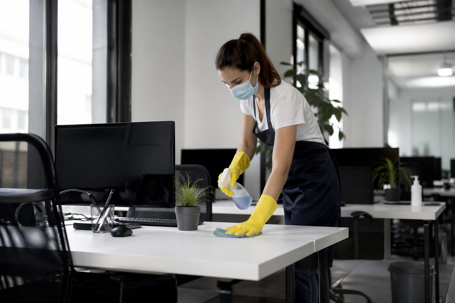 Agent d’entretien nettoyant un poste de travail dans un bureau moderne adapté au télétravail partiel