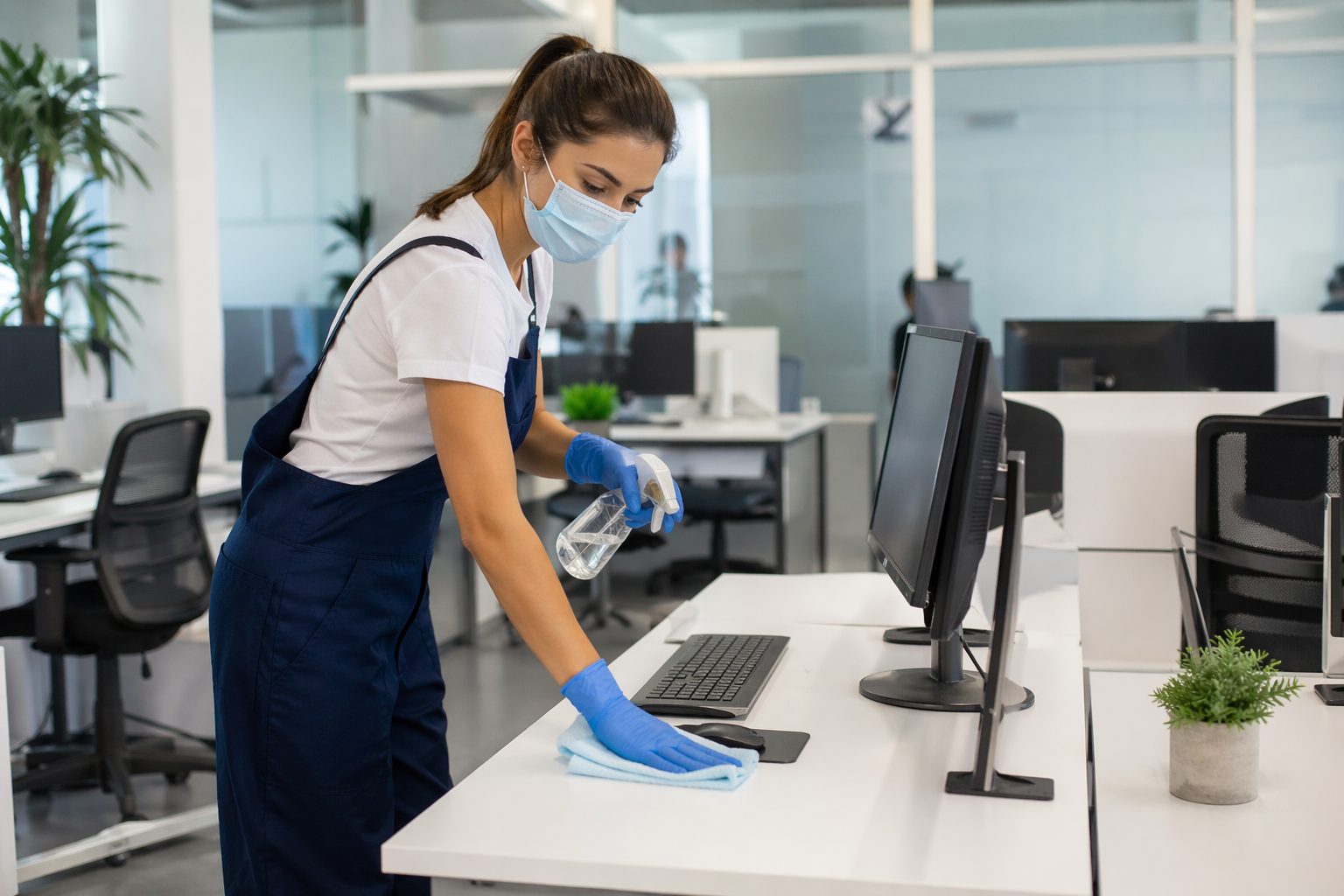 Agent d’entretien désinfectant un poste de travail dans un bureau en flex office moderne
