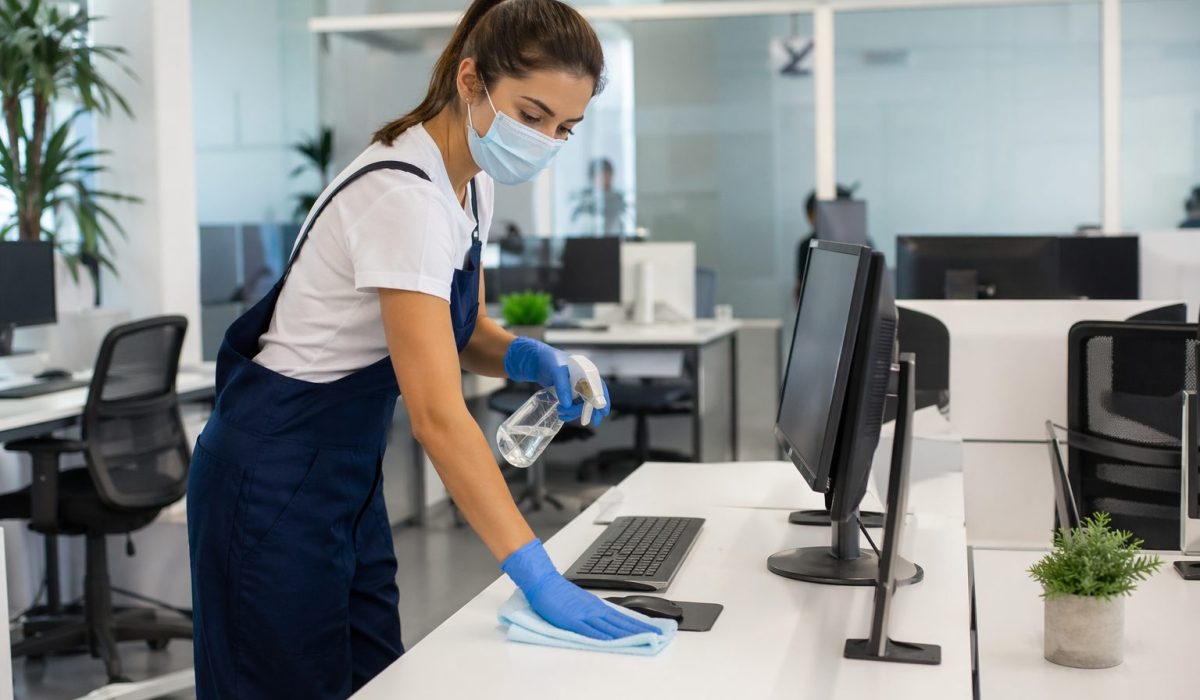 Agent d’entretien désinfectant un poste de travail dans un bureau en flex office moderne