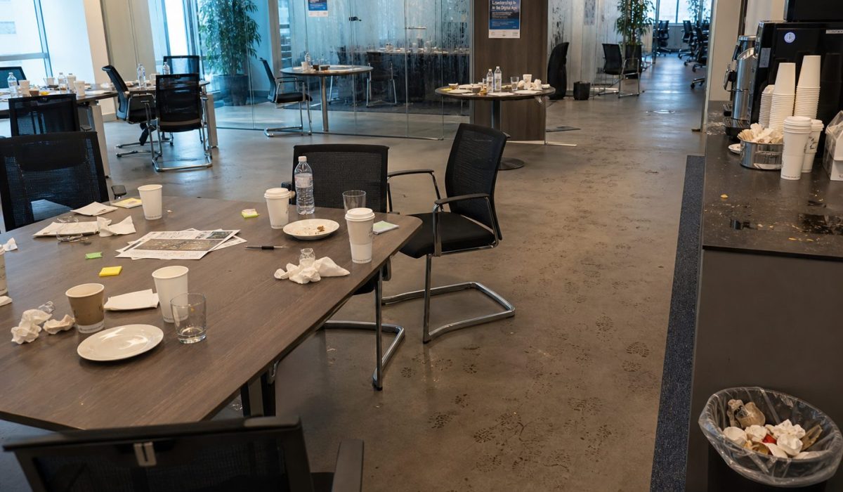 Bureaux professionnels en désordre après un séminaire avec tasses, papiers, traces au sol et poubelle remplie